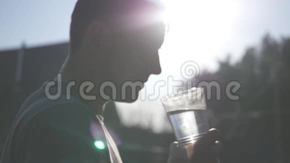 一个年轻人从杯子里喝干净的水水滴沿着底部流动在阳光下发光慢慢视频的预览图
