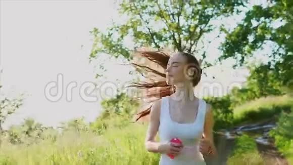 年轻快乐微笑的女人在大自然上慢跑她听音乐视频的预览图