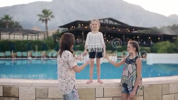 有两个女儿的幸福母亲拥抱和享受生活背景中有一个游泳池视频的预览图