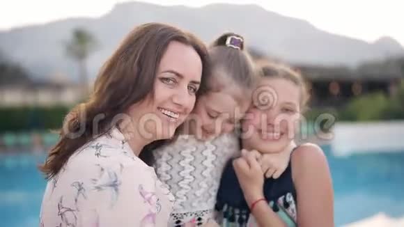 泳池背景下幸福的母亲和两个女儿的画像视频的预览图