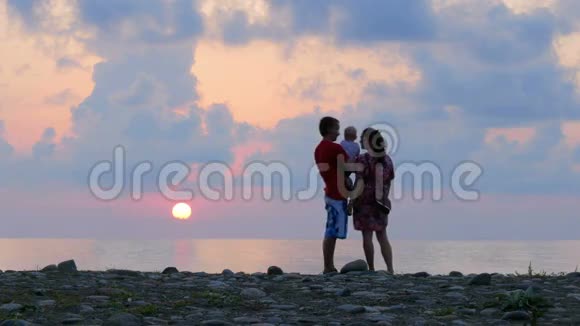 希斯利瓦亚一家人日落时父亲母亲小儿子在岩石海边父母在里面玩和亲吻宝宝视频的预览图