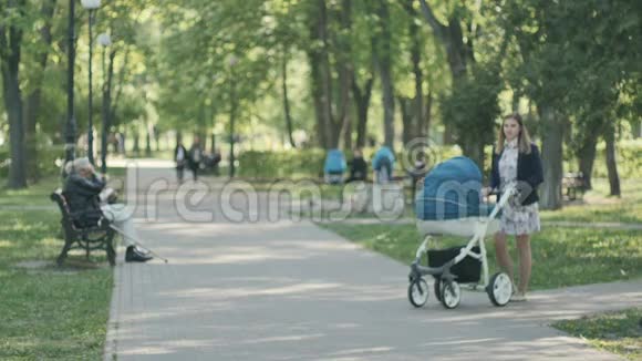 带着婴儿车的年轻妈妈在绿色公园散步视频的预览图