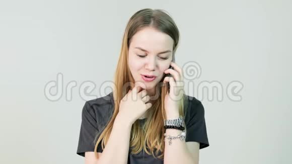年轻的女人微笑着在白色的背景上用手机说话一位年轻的休闲女士的正面景色视频的预览图