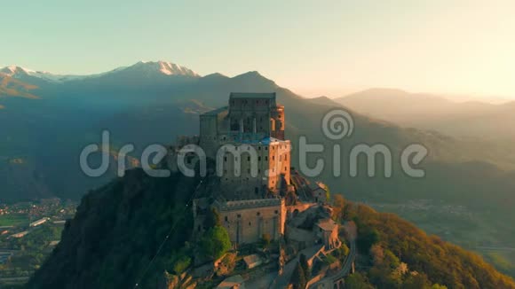 空中飞行无人机飞在古老的中世纪修道院栖息在山顶令人惊叹的背景雪阿尔卑斯山在日出圣萨克拉视频的预览图