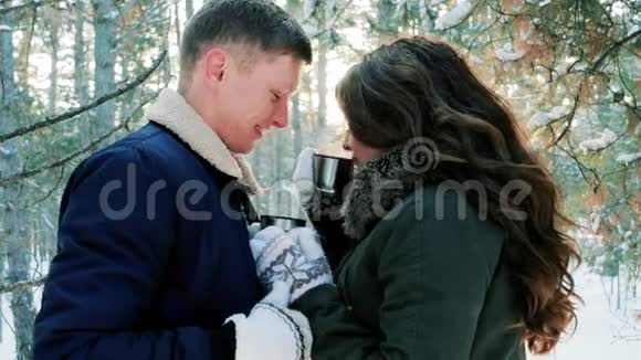 男人和女人从杯子里喝茶在冬天的森林里喝咖啡年轻人亲吻一个美丽的女人一对相爱的人视频的预览图