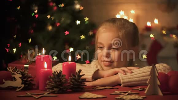 小女孩看着桌子上的圣诞装饰品树上的灯光闪烁视频的预览图