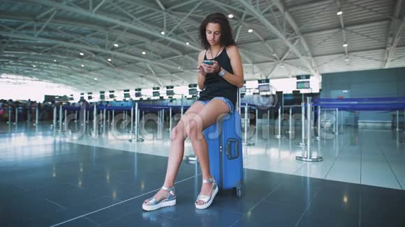 乘客机场里的女人在等她的航班在她的电话里查看留言并回忆起她的旅行视频的预览图