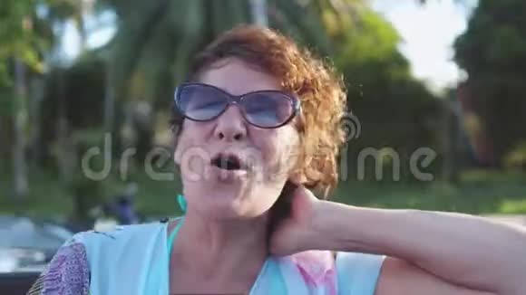 相当成熟的女人戴着太阳镜享受夏天的阳光快乐的微笑女人在风中旅行视频的预览图