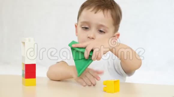 一个孩子在玩彩色积木盖房子坐在白色背景的桌子旁孩子和玩具视频的预览图