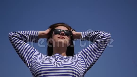 年轻漂亮的女孩穿着一件条纹衬衫享受阳光和炎热在一根清澈的蓝色头发上飘飘然视频的预览图