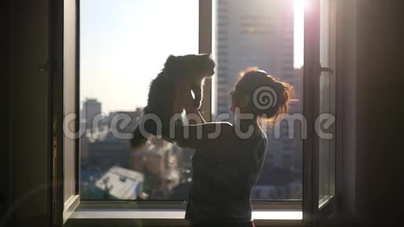 女孩手里拿着一只毛茸茸的猫站在敞开的窗户旁边在他的背景下旋转视频的预览图