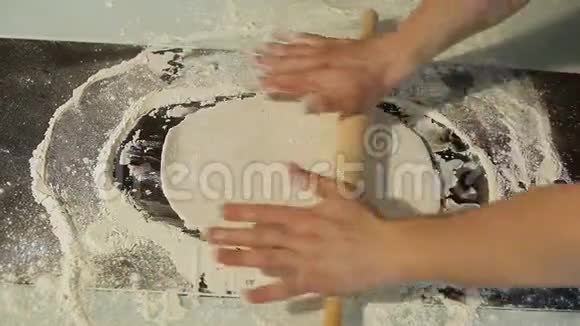 人用擀面杖把面团擀在厨房的桌子上视频的预览图