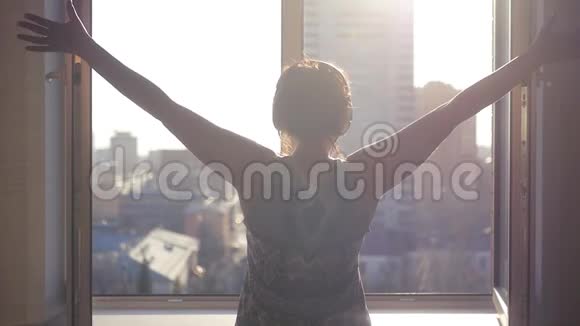 窗前的女孩在快乐的春天阳光下举起双手听耳机上的音乐慢动作1920x1080视频的预览图