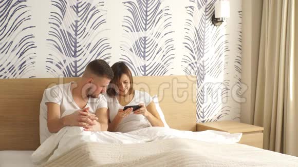 带着智能手机躺在床上微笑的夫妇视频的预览图