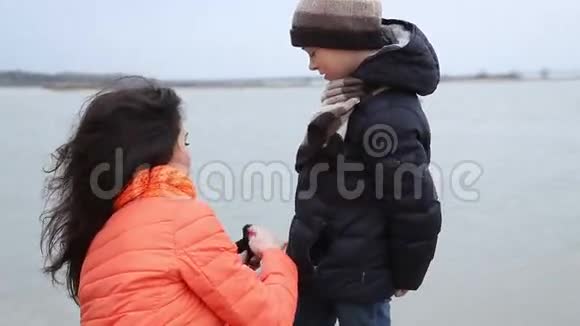 河岸上的娱乐活动妈妈把帽子和围巾伸直给儿子视频的预览图