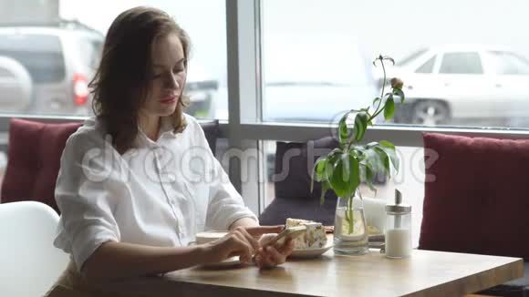 一个女孩坐在咖啡馆里用手机一个年轻的女人用手机和喝咖啡发信息视频的预览图