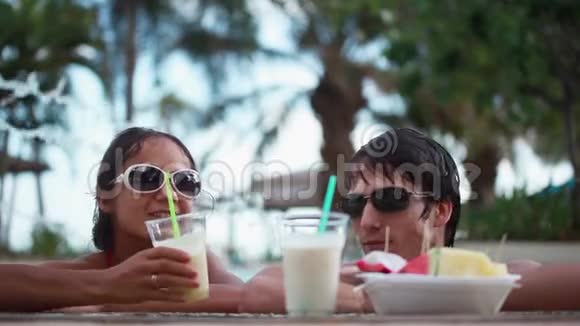 一对戴墨镜的夫妇在游泳池里度假喝酒1920x1080视频的预览图