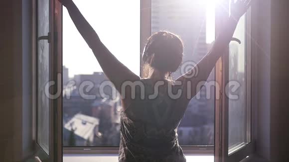 一个年轻漂亮的女孩站在窗户附近在城市风景的背景下用阳光关上了睫毛视频的预览图