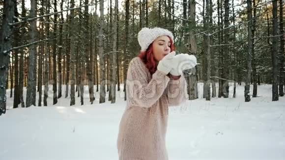 美丽的女孩吹着雪雪花飞舞快乐的肖像微笑的红发的女孩在一片雪林中视频的预览图