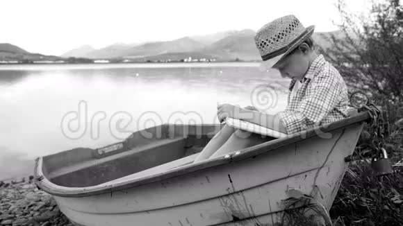 黑白镜头一个男孩坐在木船上看书视频的预览图