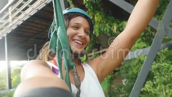 年轻快乐的女人戴着头盔在美丽的热带森林的丛林上滑上了高空滑索慢动作1920x1080视频的预览图
