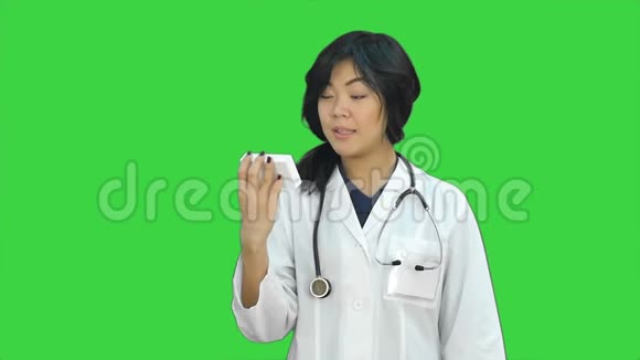 漂亮的亚洲女医生穿着实验室外套用听诊器在绿色屏幕上用手机说话Chroma键视频的预览图