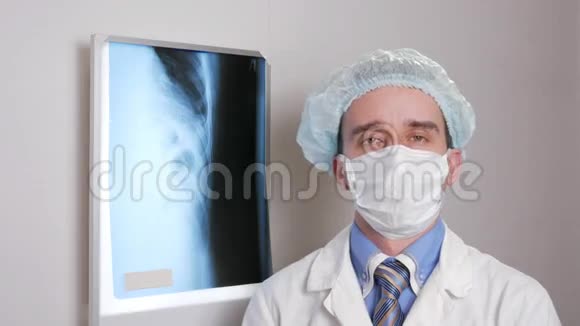 一个戴着面罩的年轻医生看着相机微笑头上戴防护帽在背景下悬挂视频的预览图