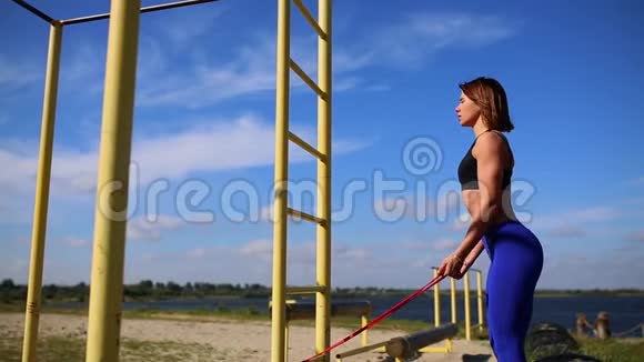 大自然上的女孩在肱二头肌上做弹性带的练习河边的户外运动视频的预览图