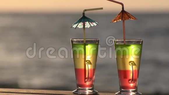 两杯鸡尾酒用吸管放在沙滩桌上背景是阳光下的大海特写视频的预览图