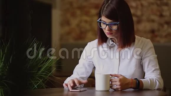 带眼镜的浅黑色混血儿喝着芬芳的咖啡用手机拨通短信看着视频的预览图