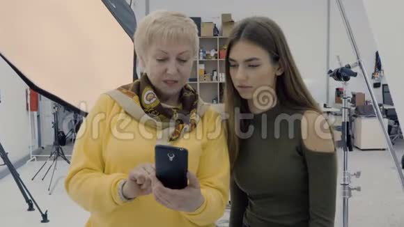 两个女人在照相馆看智能手机的照片视频的预览图