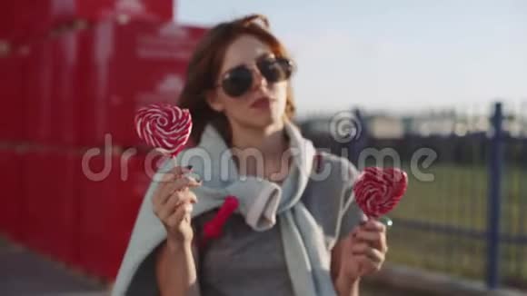 美丽的年轻快乐的女人在日落时带着两个彩色棒棒糖在街上视频的预览图