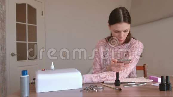 女人在紫外线灯下用紫胶擦干指甲在手机上浏览互联网视频的预览图