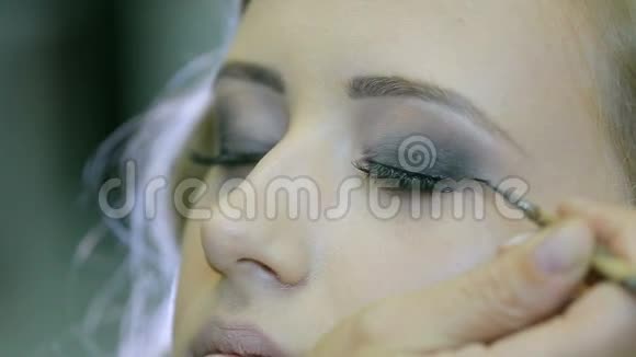 专业化妆师用眼笔和画笔在金发模特眼皮上做眼睑箭头视频的预览图