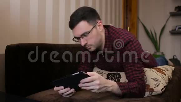 成年男子在沙发上放松看着玩游戏数字平板电脑视频的预览图