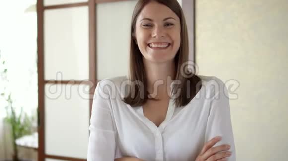 穿着白色上衣的年轻女子站在客厅微笑着双臂交叉的肖像视频的预览图