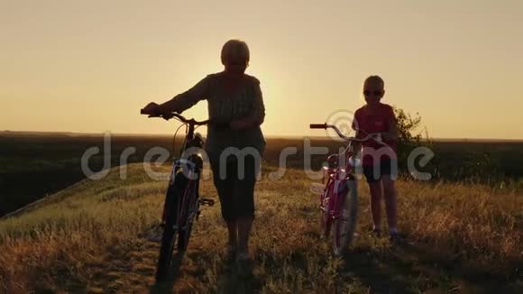 一位年迈的妇女正和孙女在农村散步他们走在旁边开着自行车视频的预览图