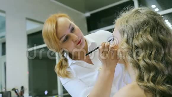 专业化妆师用眼笔和画笔在金发模特眼皮上做眼睑箭头视频的预览图