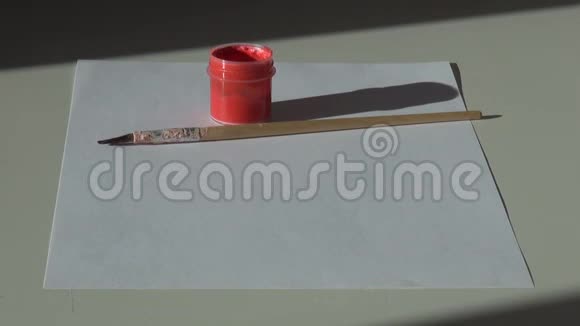 桌子上有纸刷子和一罐红色丙烯酸水粉漆视频的预览图