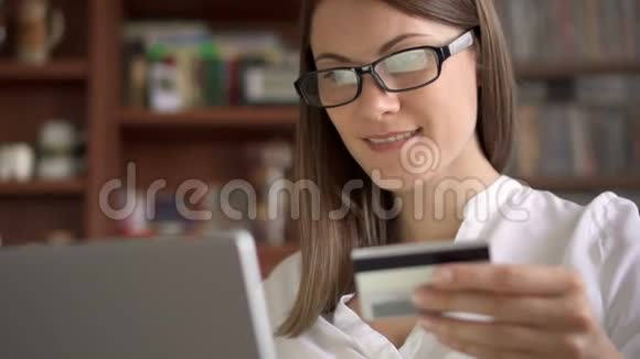 穿着白色衬衫的女商人坐在客厅的沙发上用笔记本电脑上网购买信用卡视频的预览图