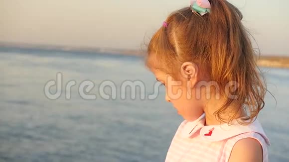 日落时分可爱的小女孩站在海边视频的预览图