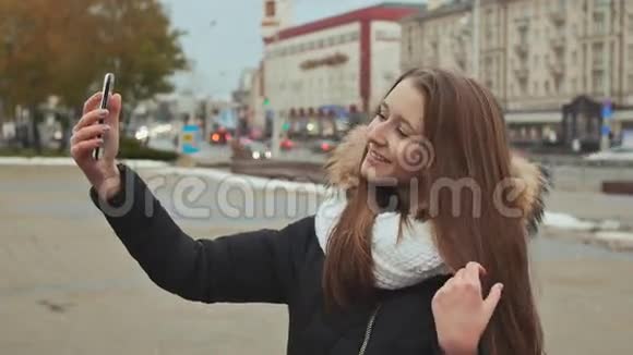 年轻漂亮的女孩穿着夹克在城市的一条街道上做自我秋天视频的预览图