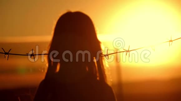 小女孩在铁丝网后面日落自由和移民的概念视频的预览图