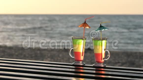 两杯鸡尾酒在木制桌面上放吸管进入海滩上的日落背景是大海视频的预览图