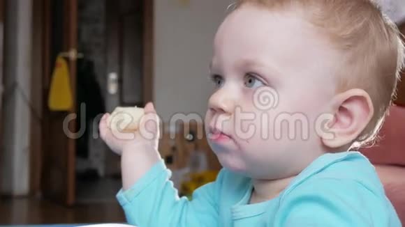 一个2岁有魅力的男孩吃香蕉在家里的桌子上仔细看电视上的卡通片视频的预览图