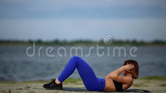 穿着蓝色衬衫的漂亮女运动员在海滩上做运动户外健身视频的预览图