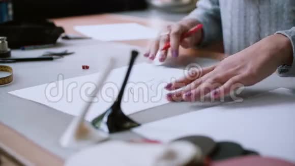 年轻女子手的特写女孩坐在桌子旁用铅笔在纸上画鞋子的草图4K视频的预览图