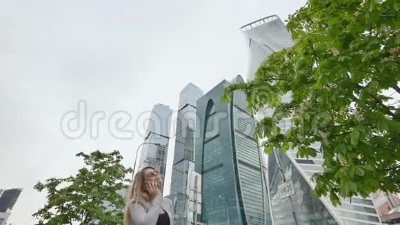 在市中心摩天大楼和高楼大厦的背景下一个金发女孩正在打电话视频的预览图