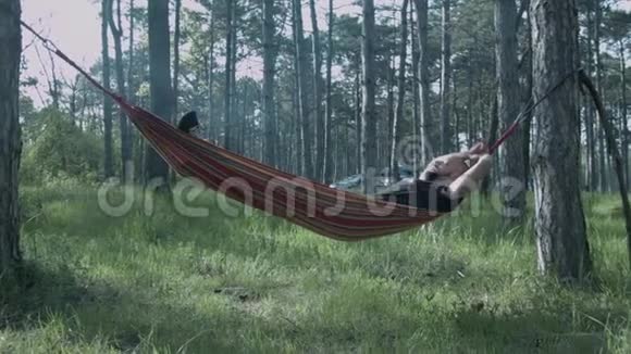 一个年轻人睡在森林里的吊床上游客正躺在吊床上视频的预览图