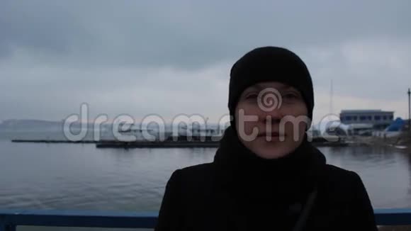 冬天阴天码头上一个穿黑色裙子的女孩的肖像视频的预览图